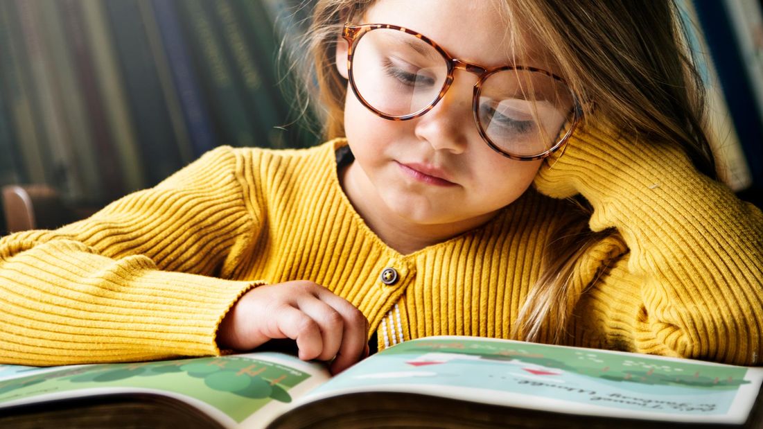 A young girl with glasses reading a book