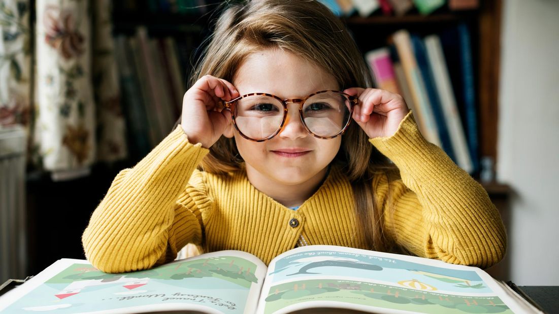 A girl putting on glasses to read a booko