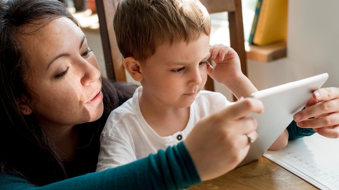 A boy being shown to use a tablet by a speech therapist 