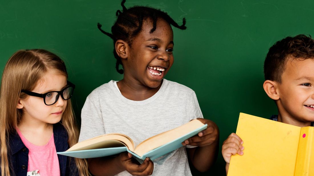 A group of kids reading a book and smiling